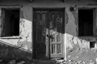 Weathered wooden door with bullet damage in abandoned desert building, harsh sunlight casting long shadows