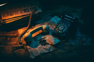 Vintage telephone handset rests beside crumpled newspapers on weathered wooden surface with dramatic shadows