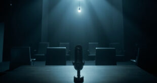 Dark broadcast studio with empty interview desk, microphone, and vacant chairs under dim overhead lighting