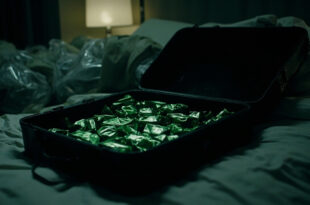Open black suitcase on hotel bed containing multiple green foil packages arranged in rows