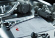 Automotive tools and car parts on steel workbench in professional garage setting with price documentation.