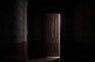 A heavy wooden door slightly ajar in a dim hallway with vintage wallpaper, light filtering through the gap