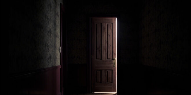 A heavy wooden door slightly ajar in a dim hallway with vintage wallpaper, light filtering through the gap