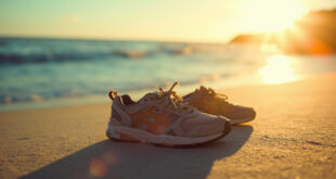 Small worn sneakers on beach sand beside calm ocean waves at sunset, symbolizing journey and recovery