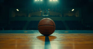 Single basketball on polished gymnasium floor under overhead lights with memorial ribbons visible on bleachers