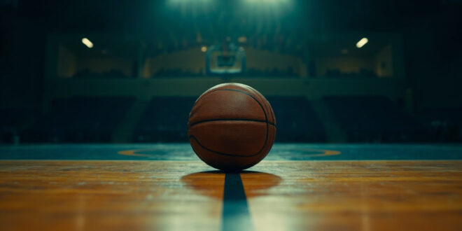 Single basketball on polished gymnasium floor under overhead lights with memorial ribbons visible on bleachers