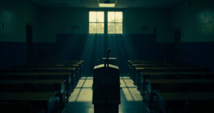 Empty wooden podium with microphone in high school auditorium, state seal on front panel, desks in background.