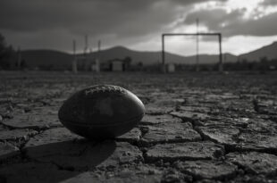 Worn football on dusty ground in empty schoolyard with distant hills under gray sky