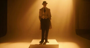 Vintage menswear suit with vest, tie and wide-brimmed hat displayed on stand against dark theatrical backdrop