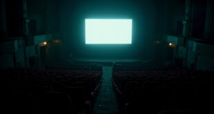 Empty cinema auditorium with red seats facing bright screen in darkness