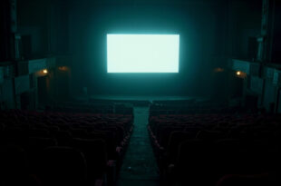 Empty cinema auditorium with red seats facing bright screen in darkness