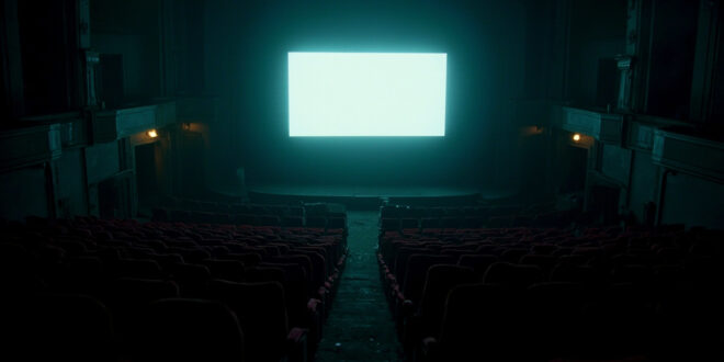 Empty cinema auditorium with red seats facing bright screen in darkness