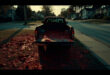 Open truck tailgate with red painted objects scattered across suburban lawn in evening light