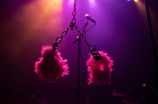 Pink fluffy handcuffs suspended in purple concert lighting beside microphone stand on dark stage
