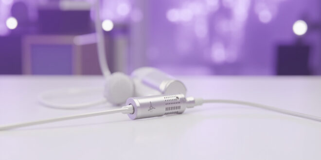 Medical port device positioned next to vintage microphone on clean white surface with purple stage lighting in background