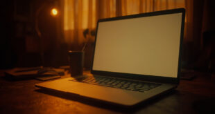 Laptop with glowing screen on wooden desk in warm evening light with paper and pen nearby