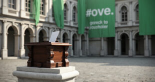 Wooden ballot box sits on marble pedestal in Gothic city hall chamber with green banners