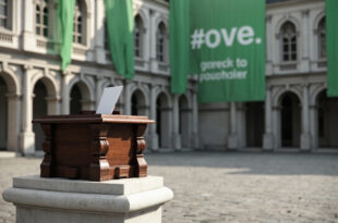 Wooden ballot box sits on marble pedestal in Gothic city hall chamber with green banners
