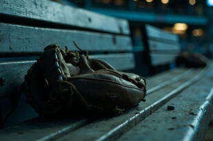 Solitary baseball glove on wooden dugout bench with soft stadium lighting in background