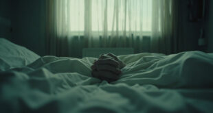 Two hands clasped together on white hospital bedding in a quiet medical room.