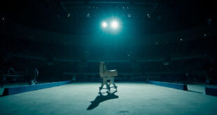 Empty gymnastics floor mat under bright spotlight in large arena with no competitors present