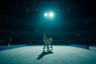 Empty gymnastics floor mat under bright spotlight in large arena with no competitors present
