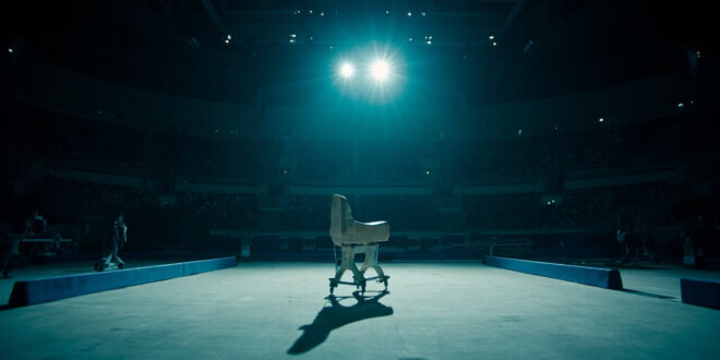 Empty gymnastics floor mat under bright spotlight in large arena with no competitors present
