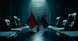 Two national flags crossed on polished wooden conference table in austere government office setting