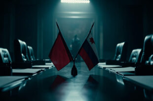 Two national flags crossed on polished wooden conference table in austere government office setting