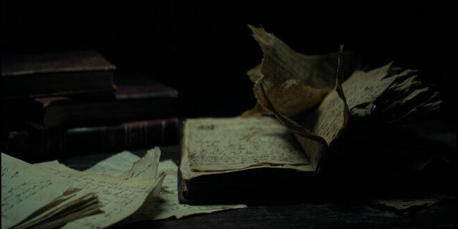 Open book with torn pages scattered on dark wooden desk beside ink-stained quill and crumpled letters