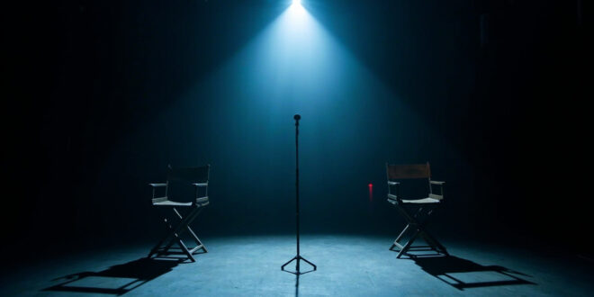 Empty television studio with microphone stand and two vacant chairs under dramatic stage lighting in darkness