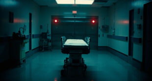 Hospital gurney in empty corridor facing closed operating room doors with overhead surgical lights