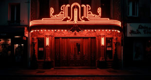 Illuminated Parisian cabaret theater entrance at night with red velvet curtains and ornate facade against dark sky