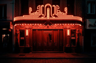 Illuminated Parisian cabaret theater entrance at night with red velvet curtains and ornate facade against dark sky