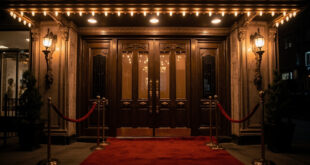 Historic theater entrance with ornate brass doors and glowing marquee lights against burgundy velvet backdrop