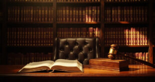 Wooden gavel on sound block next to leather law books on polished desk in traditional courtroom setting