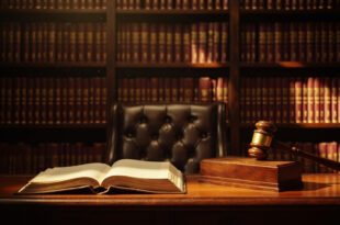 Wooden gavel on sound block next to leather law books on polished desk in traditional courtroom setting