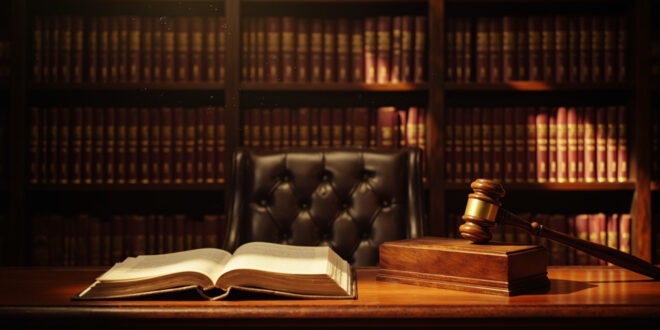 Wooden gavel on sound block next to leather law books on polished desk in traditional courtroom setting