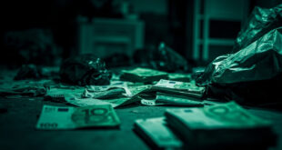 Stacks of one hundred euro banknotes on table with evidence bags in dim room under harsh overhead light