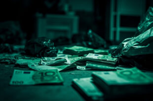Stacks of one hundred euro banknotes on table with evidence bags in dim room under harsh overhead light