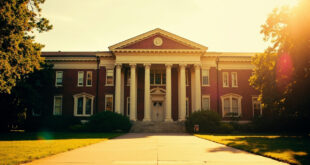 Historic brick university building with white columns standing majestically on empty campus quad under clear sky