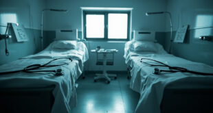 Two empty hospital beds with medical equipment and folded white linens under fluorescent lighting in clinical rooms