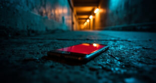 Smartphone with glowing red alert screen in dark concrete bunker corridor illuminated by amber emergency lights