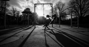 Overturned chair on empty concrete schoolyard, playground equipment silhouetted against overcast sky