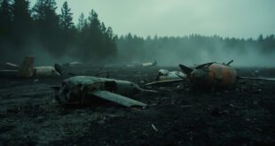 Broken military drone parts lying on ground near forest with testing equipment in background