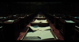 Scattered official documents and folders on dark wooden parliamentary desk in empty government chamber