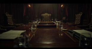 Empty diplomatic meeting room with wooden conference table, scattered papers, and formal chairs in dim lighting.