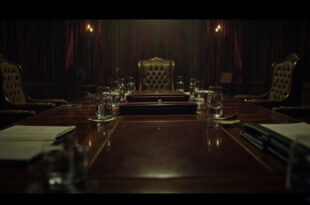 Empty diplomatic meeting room with wooden conference table, scattered papers, and formal chairs in dim lighting.
