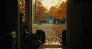 Two school backpacks and luggage beside a wooden front door in autumn setting