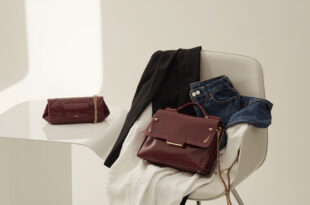 Burgundy leather handbag with gold chain beside white fabric and blazer on neutral minimalist background